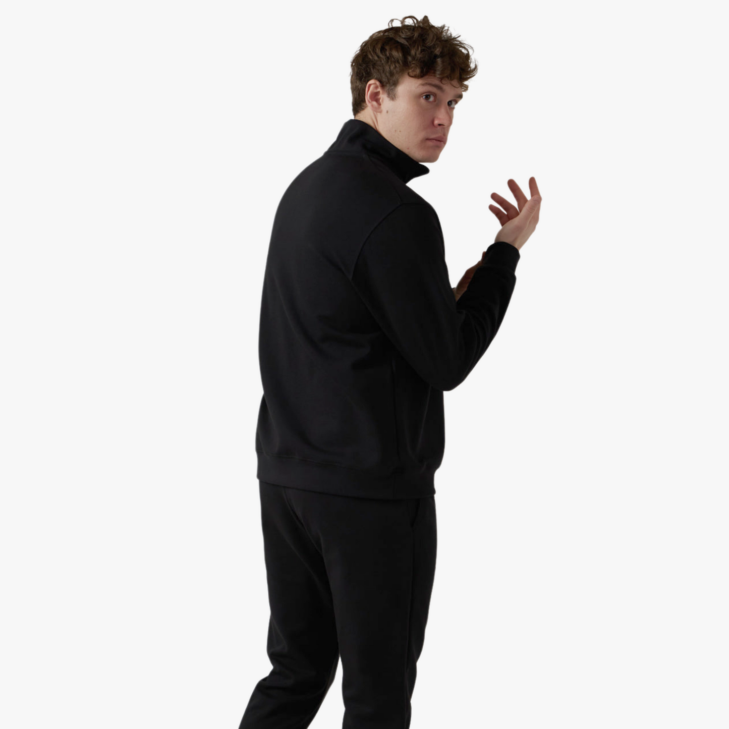 Male model wears black half zip set and poses while fixing sleeve
