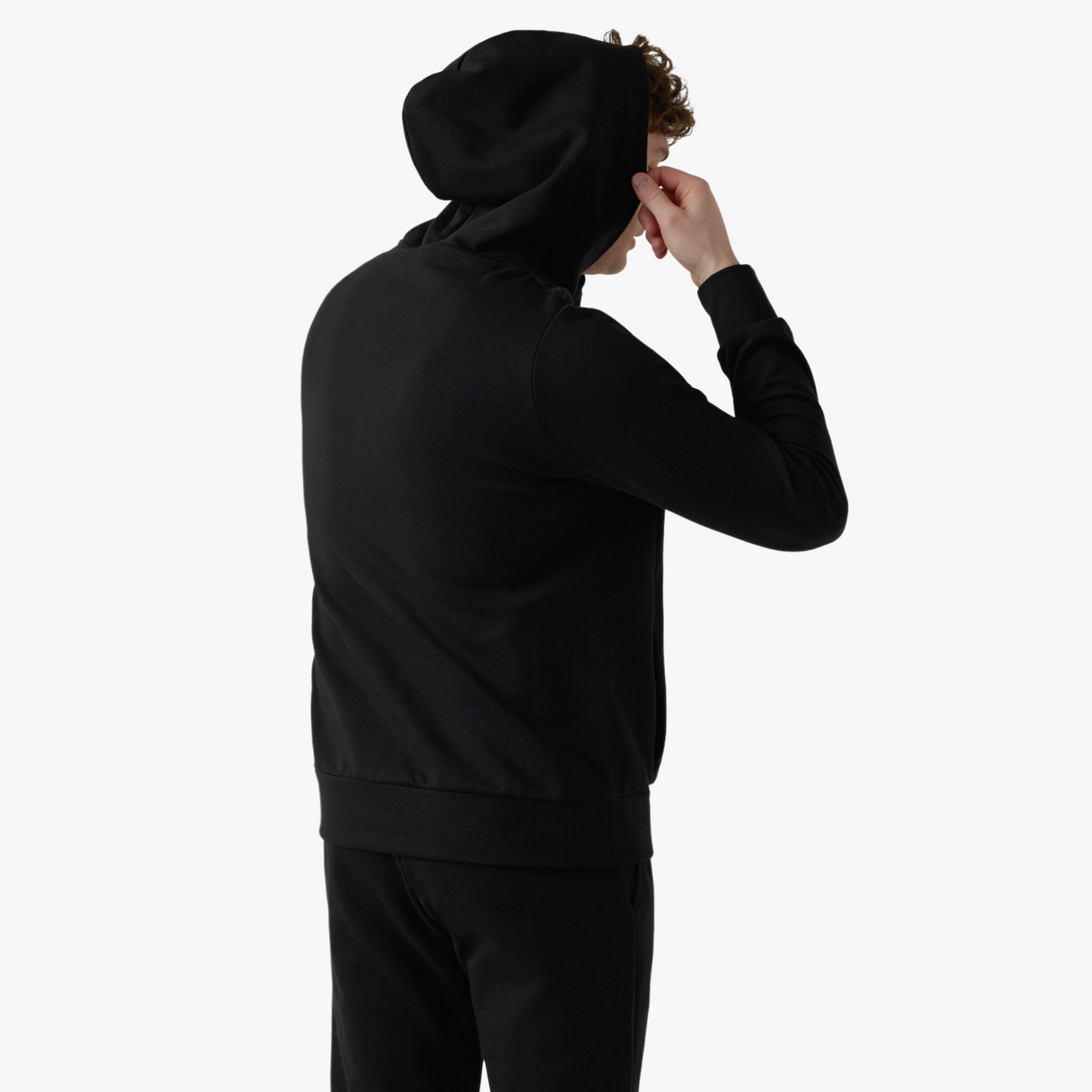 Male model wears black classic set and holds hood upwards
